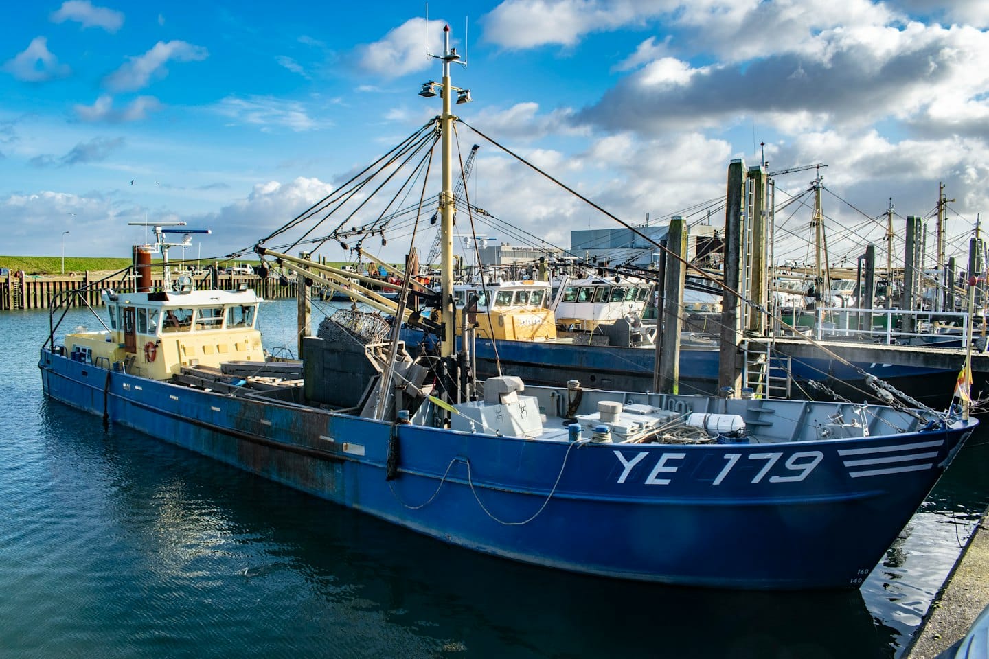 Blue fishing trawler docked at a busy harbor.