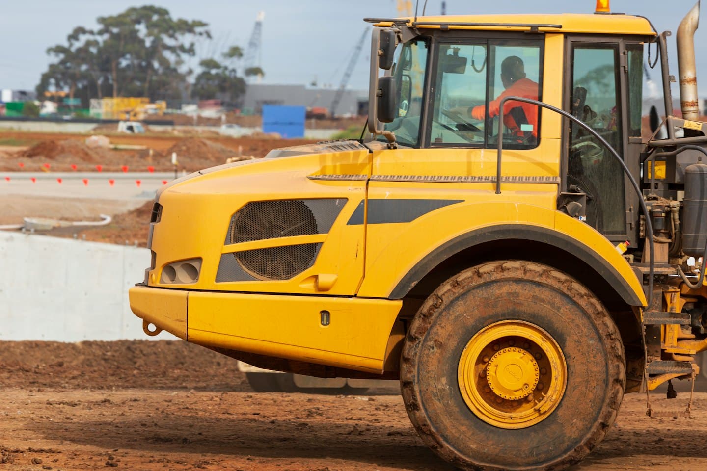 Worker operates a yellow dump truck on a construction site.