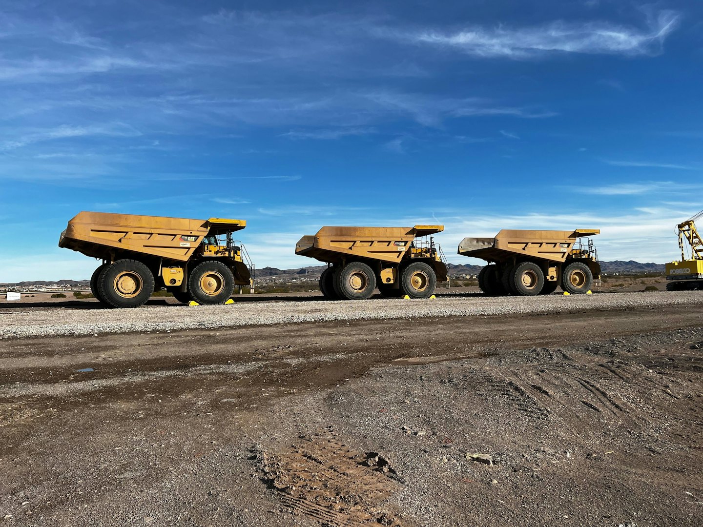 Three yellow dump trucks parked at a large construction site.