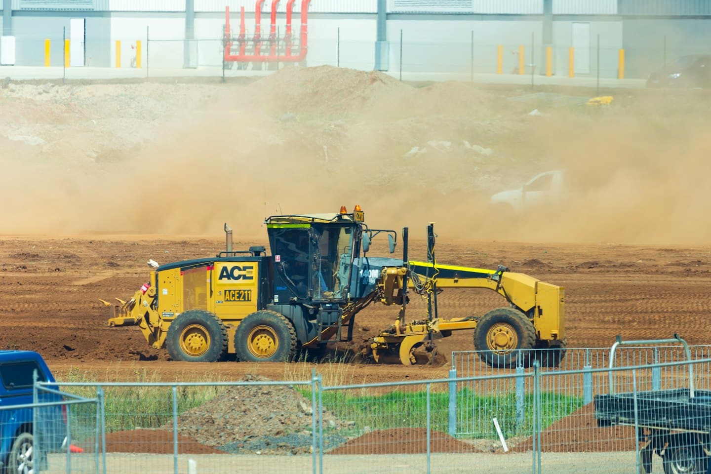 Yellow motor grader levels dusty earth on construction site.