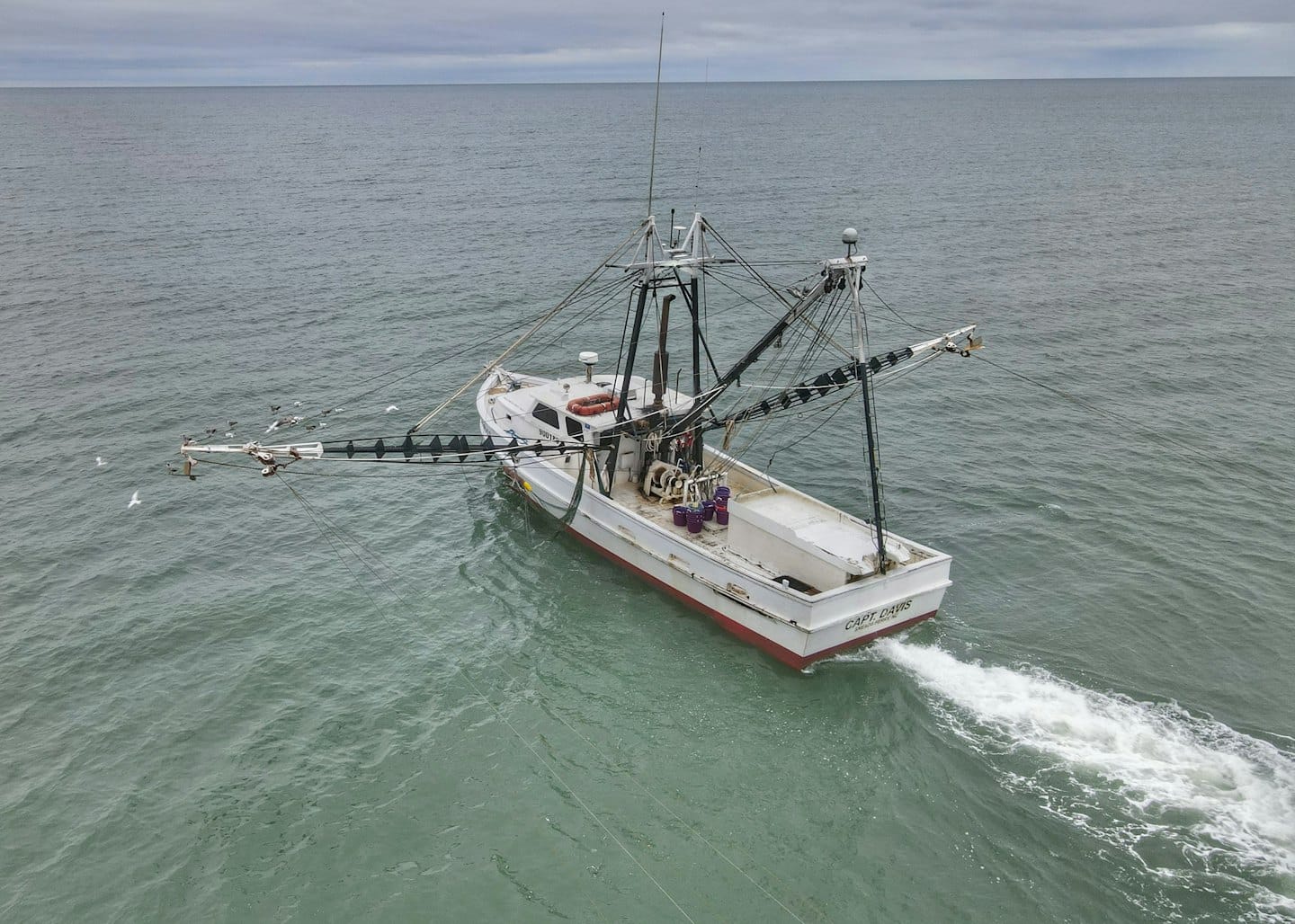 White fishing trawler with red trim navigating choppy ocean waters.